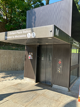 A picture of a WMATA elevator. The door to the elevator is slightly to the right of center for the image and past the elevator there is a retaining wall. The elevator has an overhand that is about 2/3 of the way up the image.